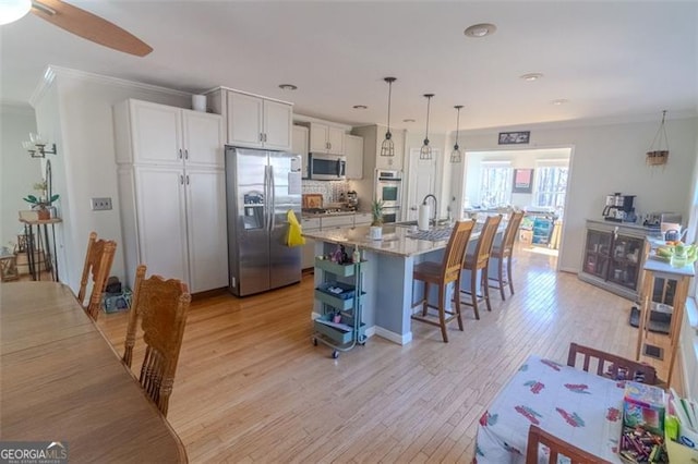 kitchen with pendant lighting, white cabinetry, stainless steel appliances, light stone countertops, and a center island with sink