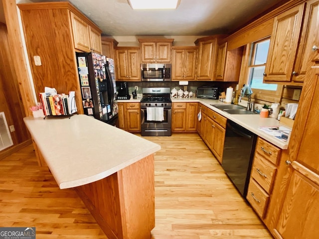 kitchen featuring sink, a breakfast bar area, light hardwood / wood-style floors, and black appliances