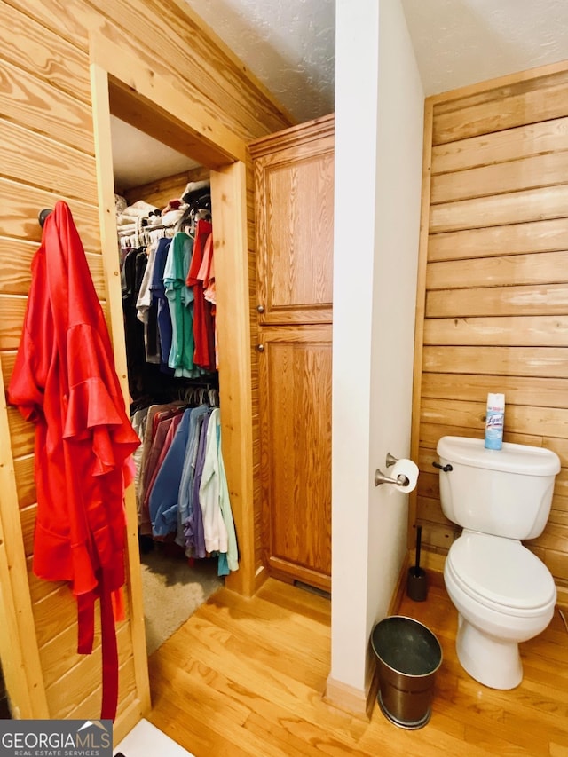 bathroom with wood-type flooring, wooden walls, and toilet