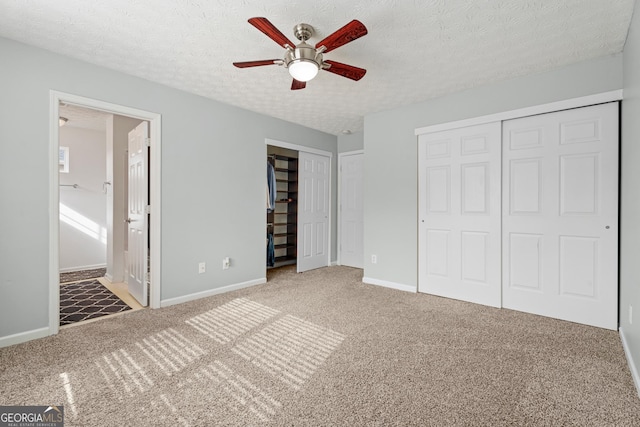 unfurnished bedroom featuring ceiling fan, ensuite bathroom, carpet, a textured ceiling, and two closets