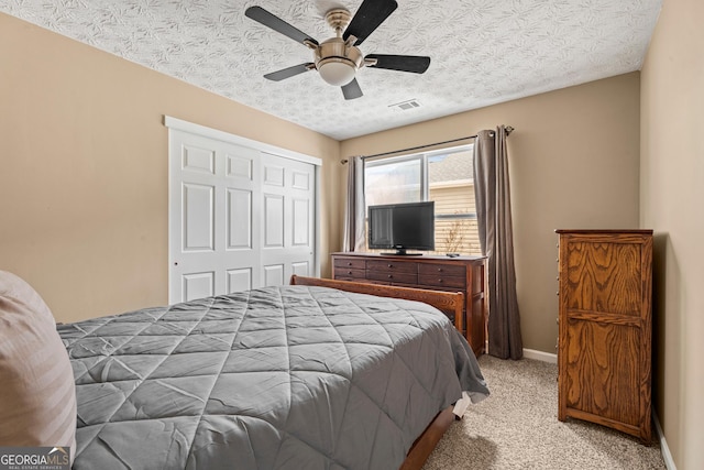 bedroom featuring ceiling fan, light colored carpet, a textured ceiling, and a closet