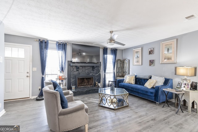 living room featuring ceiling fan, a stone fireplace, plenty of natural light, and wood-type flooring