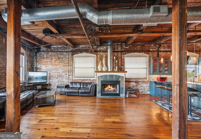 unfurnished living room with brick wall, a fireplace with flush hearth, hardwood / wood-style floors, and beamed ceiling