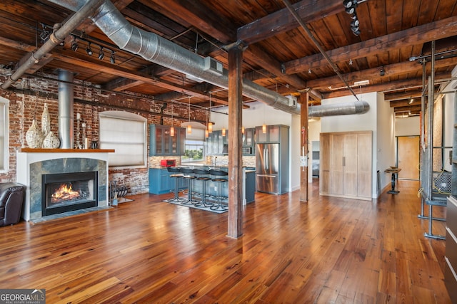 unfurnished living room featuring beam ceiling, a high ceiling, brick wall, wooden ceiling, and hardwood / wood-style flooring