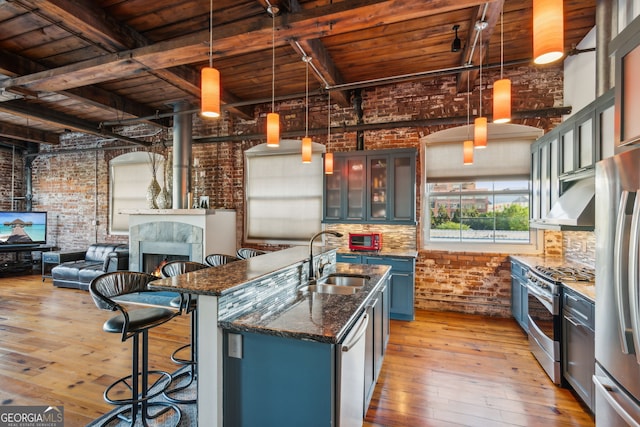 kitchen with appliances with stainless steel finishes, a sink, dark stone countertops, brick wall, and a kitchen bar