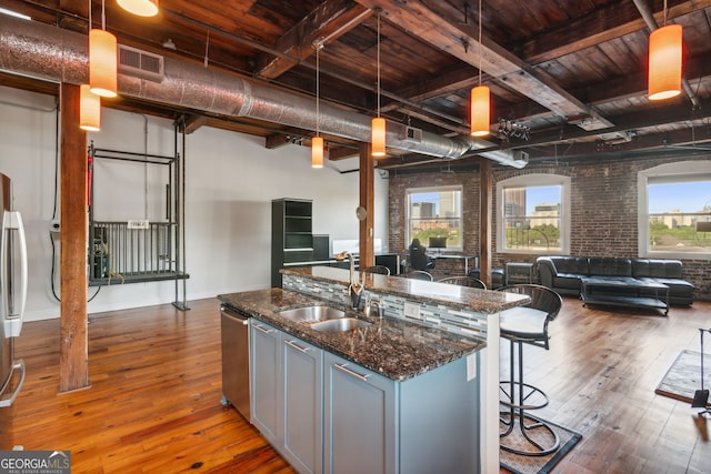 kitchen with wood-type flooring, open floor plan, a sink, brick wall, and a kitchen bar