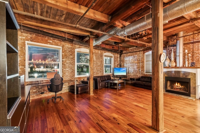 unfurnished office featuring wood-type flooring, brick wall, a tile fireplace, wooden ceiling, and beamed ceiling