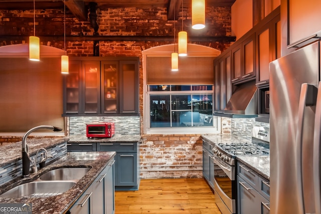 kitchen with stainless steel appliances, backsplash, light wood-style floors, a sink, and dark stone counters