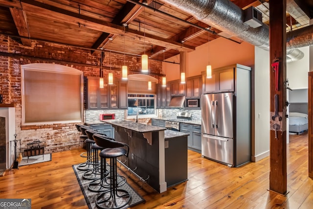 kitchen featuring stone countertops, brick wall, a high ceiling, appliances with stainless steel finishes, and light wood finished floors