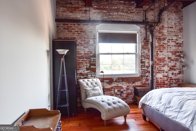 bedroom featuring brick wall and wood finished floors