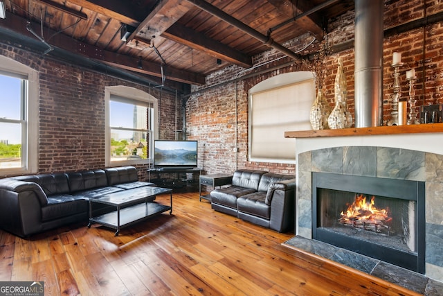 living area with hardwood / wood-style flooring, brick wall, wood ceiling, beam ceiling, and a tiled fireplace