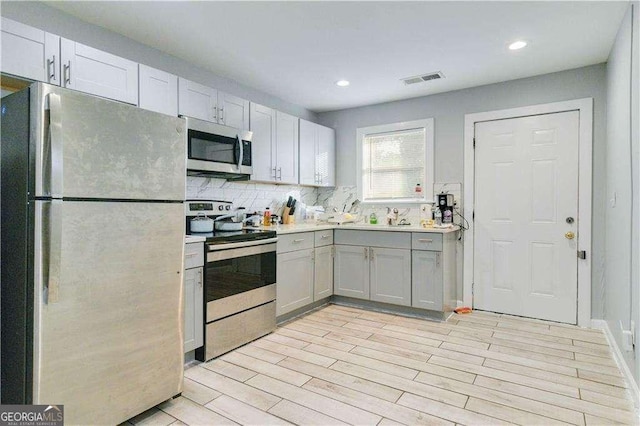 kitchen with gray cabinets, tasteful backsplash, white cabinetry, stainless steel appliances, and light wood-type flooring