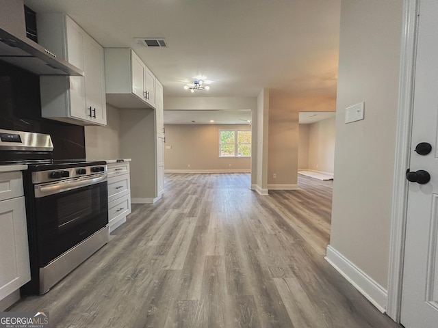 kitchen featuring wall chimney range hood, tasteful backsplash, light hardwood / wood-style floors, white cabinets, and stainless steel range with electric cooktop