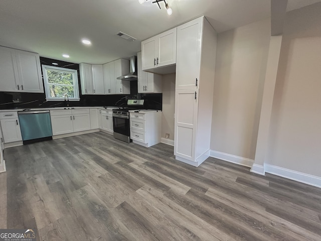 kitchen featuring white cabinetry, appliances with stainless steel finishes, wood-type flooring, and wall chimney range hood