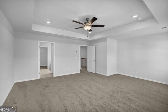 unfurnished bedroom featuring ceiling fan, a tray ceiling, carpet, and a spacious closet