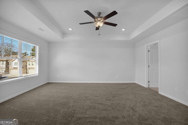 carpeted spare room with a raised ceiling and ceiling fan