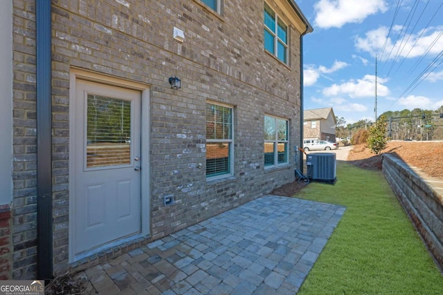 doorway to property featuring central AC unit, a patio area, and a lawn