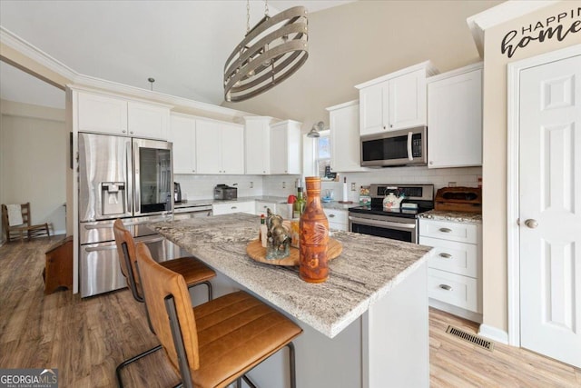 kitchen with a breakfast bar, appliances with stainless steel finishes, a center island, light stone counters, and white cabinets