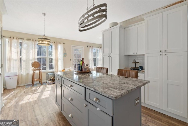 kitchen with gray cabinetry, decorative light fixtures, a kitchen island, light hardwood / wood-style floors, and white cabinets