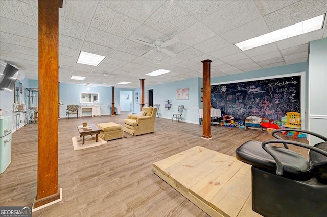 living room featuring a drop ceiling, light wood-type flooring, ceiling fan, and ornate columns