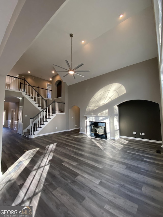 unfurnished living room featuring ceiling fan, a towering ceiling, and dark hardwood / wood-style flooring