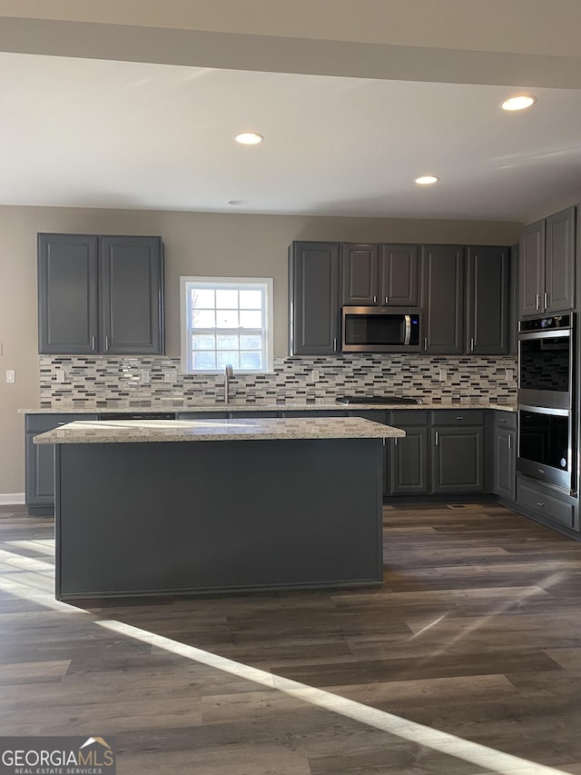 kitchen with light stone counters, dark wood-type flooring, a kitchen island, and appliances with stainless steel finishes