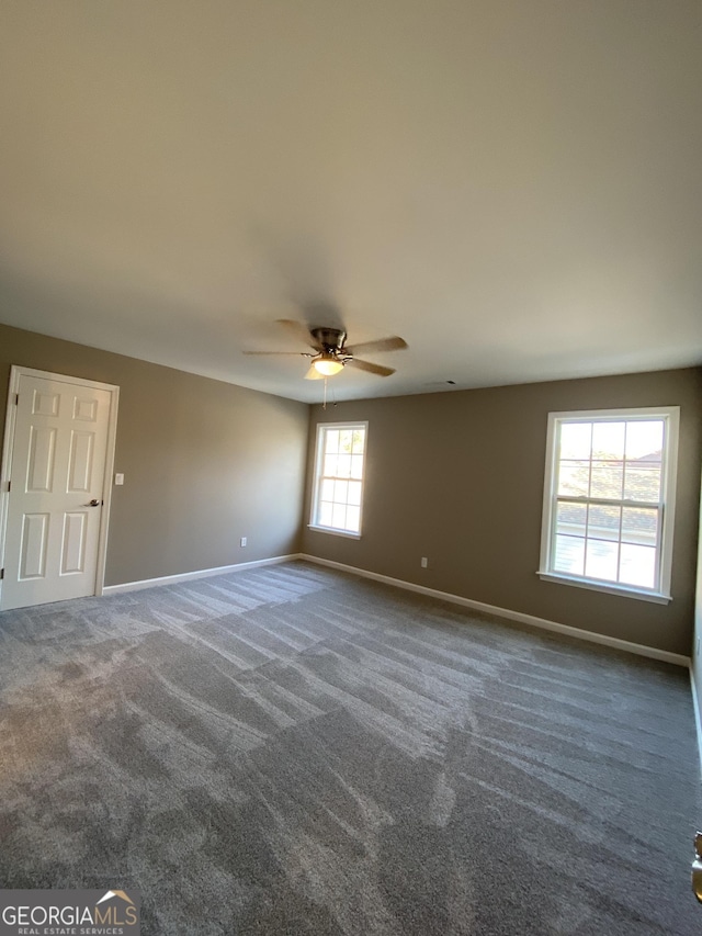 empty room with ceiling fan and dark colored carpet