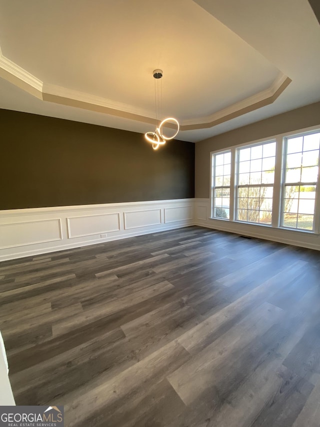 empty room with a raised ceiling, dark wood-type flooring, and a notable chandelier