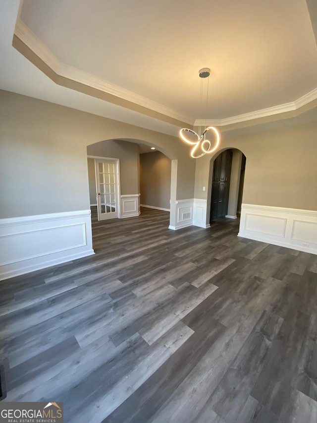 unfurnished dining area featuring ornamental molding, dark wood-type flooring, a notable chandelier, and a tray ceiling