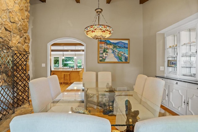 dining area with light hardwood / wood-style floors, beamed ceiling, and a high ceiling