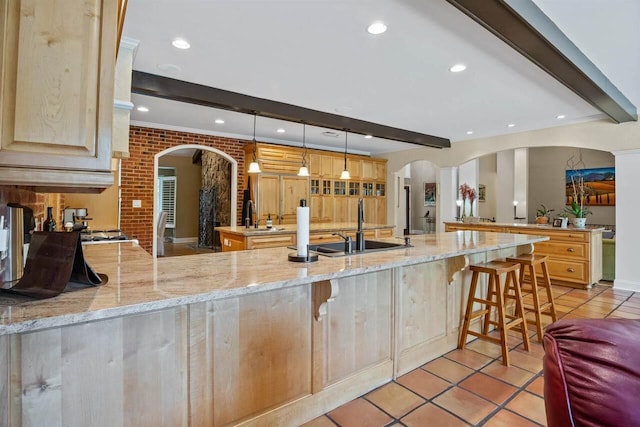 kitchen featuring light brown cabinetry, sink, kitchen peninsula, pendant lighting, and beam ceiling