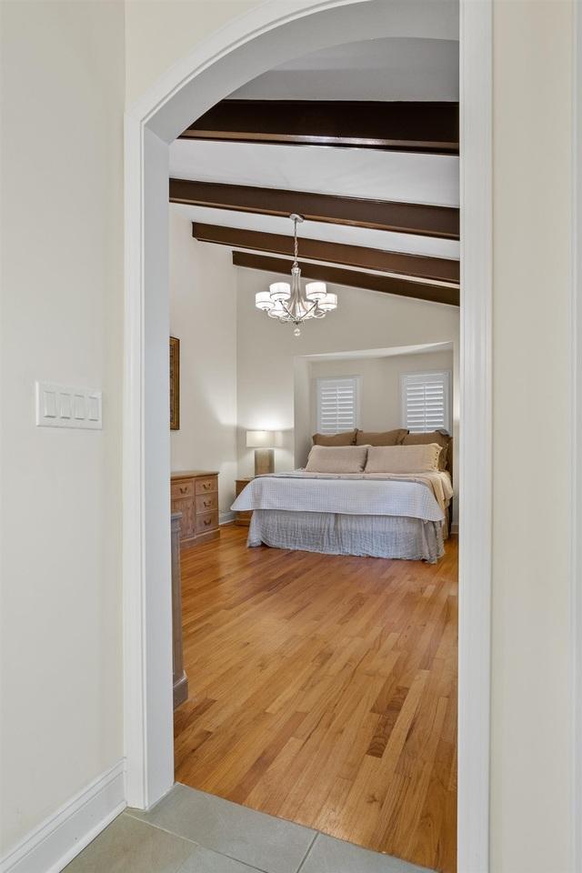 bedroom with vaulted ceiling with beams, hardwood / wood-style floors, and a chandelier