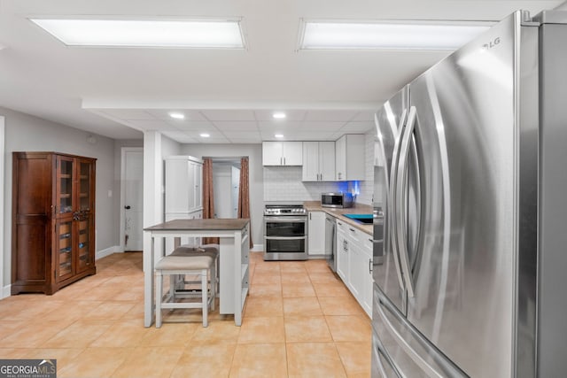 kitchen featuring white cabinets, a kitchen breakfast bar, decorative backsplash, light tile patterned floors, and stainless steel appliances