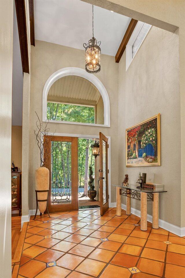 foyer with light tile patterned floors, beam ceiling, a chandelier, and a high ceiling