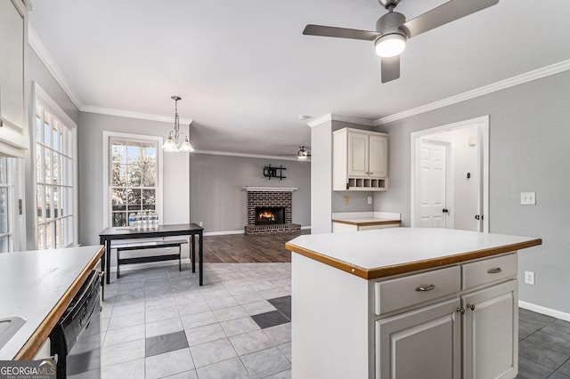 kitchen featuring a kitchen island, dishwasher, hanging light fixtures, crown molding, and a brick fireplace