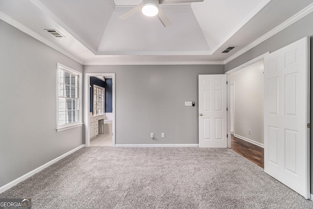 unfurnished bedroom featuring crown molding, ensuite bathroom, a tray ceiling, and carpet