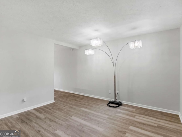 empty room with an inviting chandelier, light hardwood / wood-style floors, and a textured ceiling