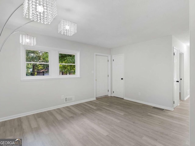 spare room featuring an inviting chandelier and light wood-type flooring