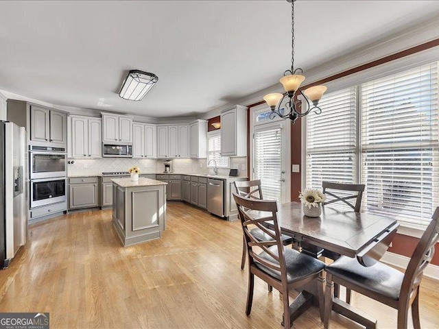 kitchen with light hardwood / wood-style flooring, appliances with stainless steel finishes, gray cabinetry, a center island, and decorative light fixtures