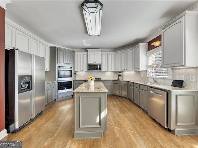 kitchen with appliances with stainless steel finishes, pendant lighting, gray cabinetry, a center island, and light wood-type flooring