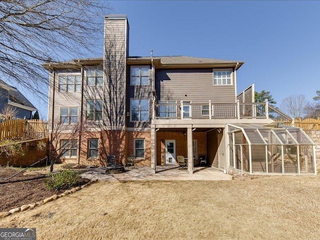 rear view of property featuring a balcony, a sunroom, a patio area, and a lawn