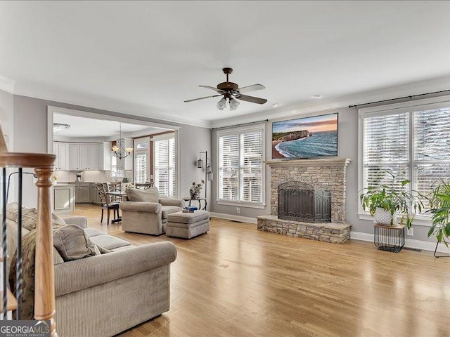 living room with light hardwood / wood-style flooring, ceiling fan with notable chandelier, a fireplace, and ornamental molding