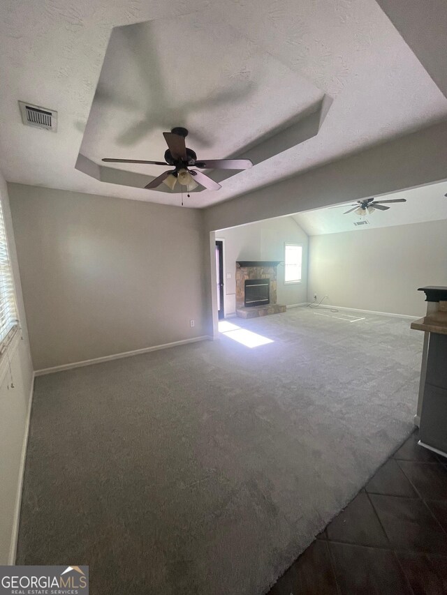 carpeted empty room featuring a raised ceiling, ceiling fan, a textured ceiling, and a fireplace