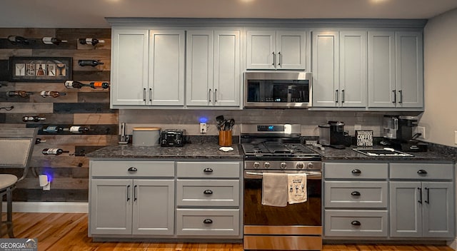 kitchen featuring appliances with stainless steel finishes, gray cabinetry, dark stone countertops, and decorative backsplash