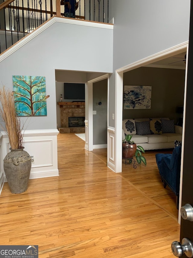 entrance foyer with a stone fireplace, a towering ceiling, ceiling fan, and light hardwood / wood-style flooring