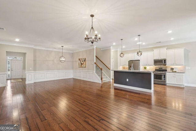 kitchen with pendant lighting, dark wood-type flooring, white cabinetry, stainless steel appliances, and an island with sink