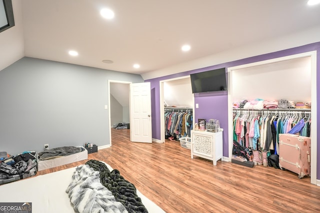 bedroom with multiple closets, wood-type flooring, and vaulted ceiling