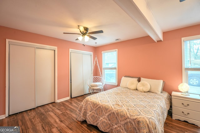 bedroom with multiple closets, dark wood-type flooring, ceiling fan, and beamed ceiling