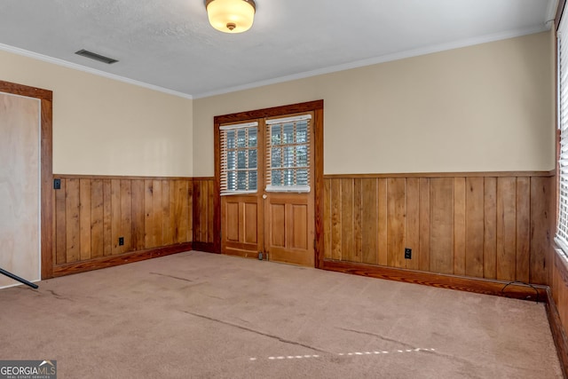 empty room featuring light colored carpet, ornamental molding, wooden walls, and a textured ceiling