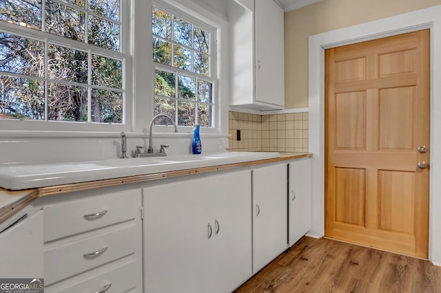 kitchen with tasteful backsplash, sink, white cabinets, and light hardwood / wood-style floors